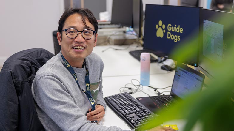 A Guide Dog employee at their desk smiles at the camera