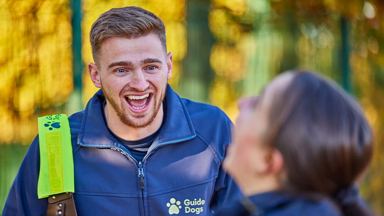 Two Guide Dogs employees laugh and smile outdoors