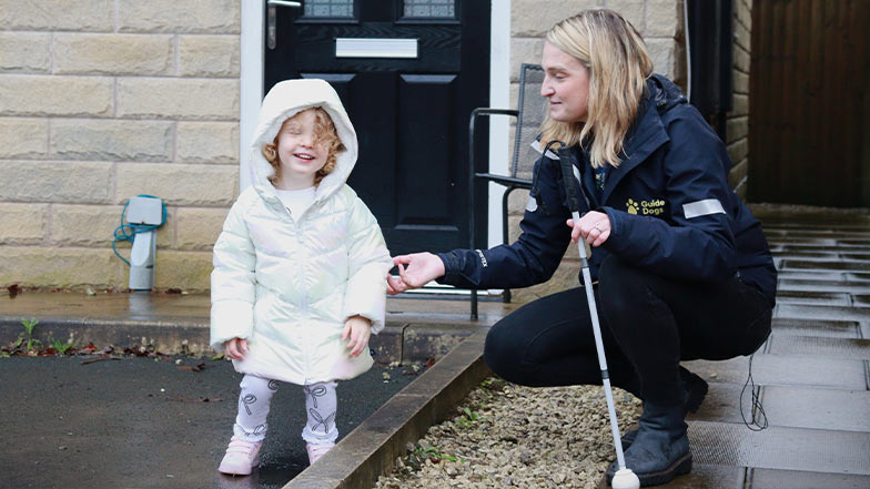 A Habilitation Specialist introduces a white cane to a young service user. They're both smiling.