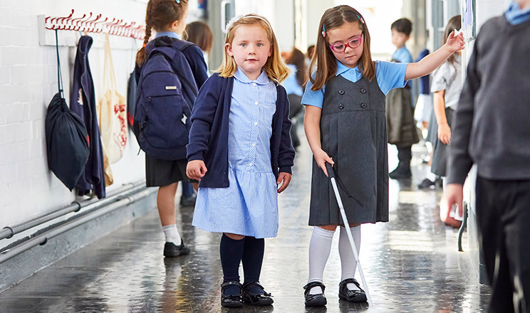 Two girls in a school corridor, one using a long cane