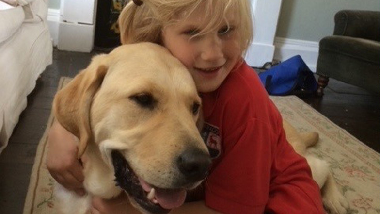 A young girl and her buddy dog cuddle in their living room, while smiling.