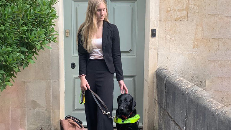 Hester, a guide dog owner, and her guide dog, Pickle, stand in front of their home.