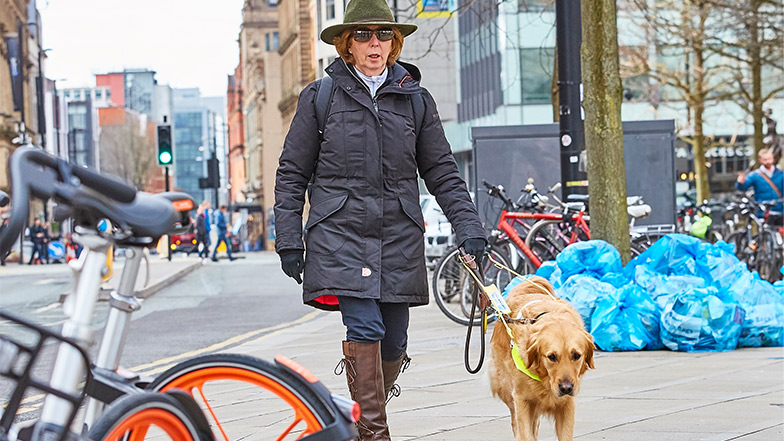 Guide dog owner and guide dog try and navigate a busy street with bicycles and rubbish around 