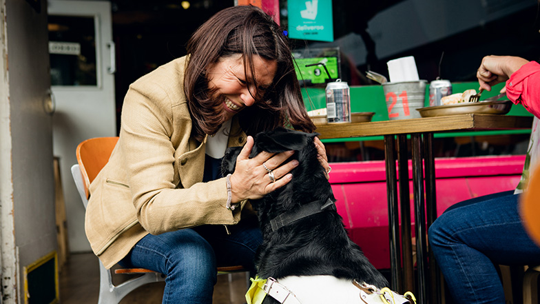 A guide dog owner hugs her black labrador dog and smiles