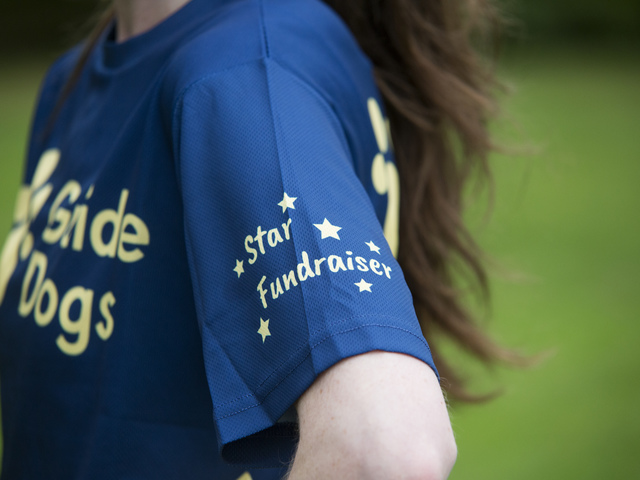A fundraiser wearing a Guide Dogs branded t-shirt which reads 'Star Fundraiser' on the arm. 