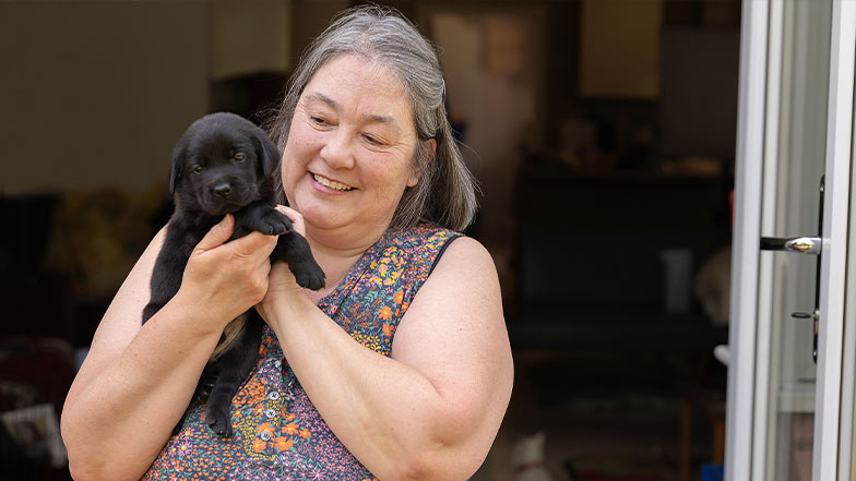 A Breeding Dog Holder smiles as she holds a black Labrador puppy.