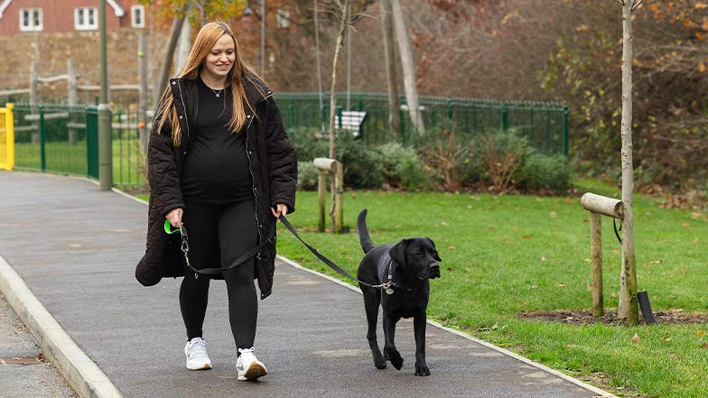 The owner of a rehomed retired guide dog smiles as she walks along the pavement with her dog.