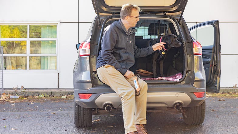 A volunteer fosterer leans against the back of his car, with a dog standing next to him in the boot.