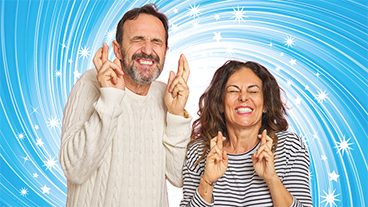 A man and a woman with their fingers crossed eyes closed smiling