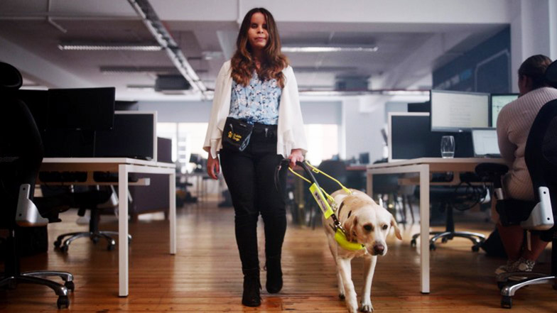 A young woman walking with her guide dog through an office