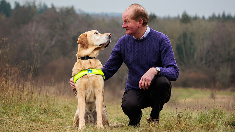 Guide dog owner crouching down next to his guide dog both looking at each other adoringly.