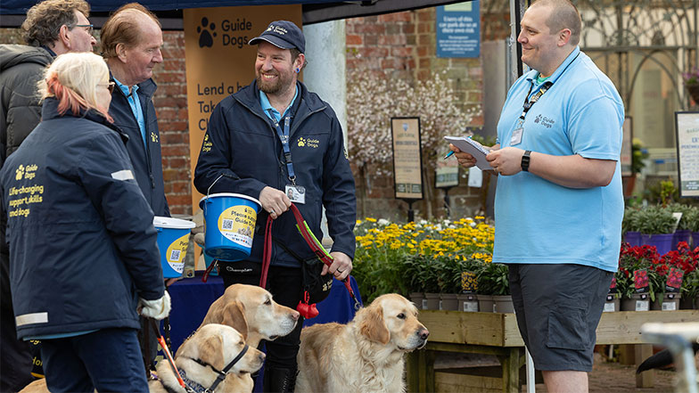 Volunteer fundraisers smile with collection boxes and guide dogs