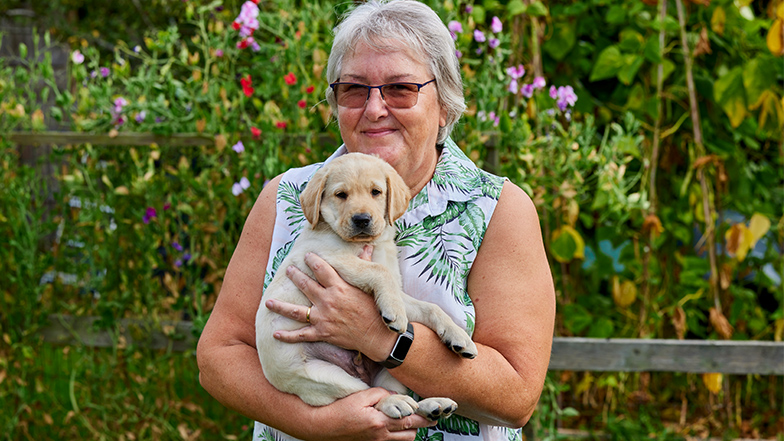 Volunteer puppy raiser Rhoda holds a guide dog puppy whilst smiling happily