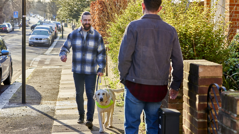 A guide dog owner and his guide dog walking along a pavement
