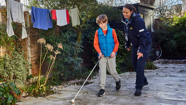 Ralph, a young service user, walks with a long cane in his garden.