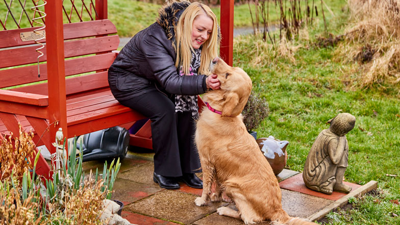 Guide dog Ringo and volunteer Louise sat on a red bench smiling at eachother.