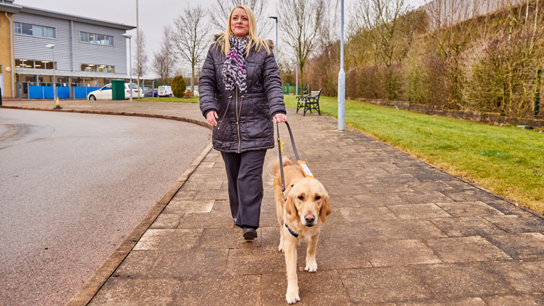 Guide dog Ringo and volunteer Louise walk along a pavement.