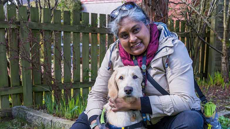 Puppy raiser, Nimmi, sitting on a garden wall cuddling her guide dog puppy