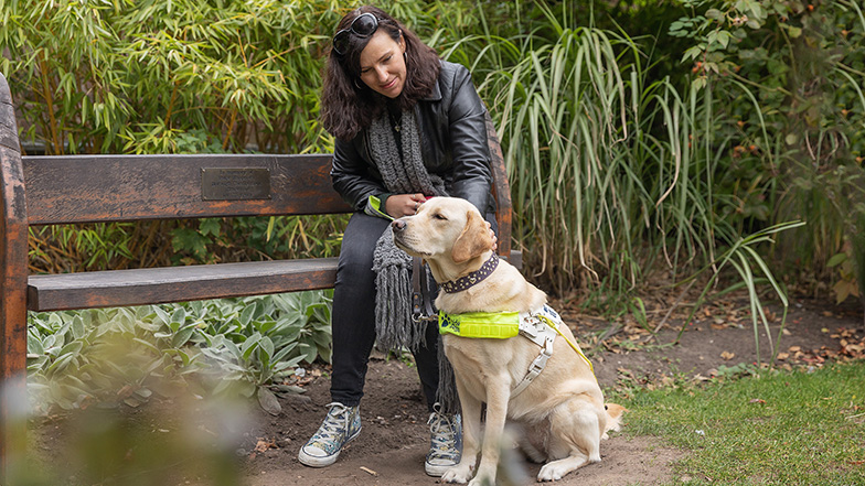 Guide dog owner Alice at a park bench with guide dog Dora