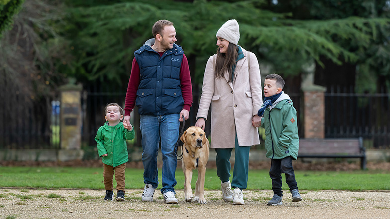 Buddy dog Cooper with six year old Alfie and his family walking together in a park