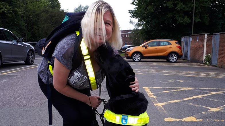 Guide dog owner Teresa stands next to black Labrador guide dog Baden