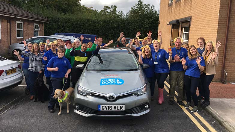 Toyota employees stood around Toyota car that was lent to Guide Dogs