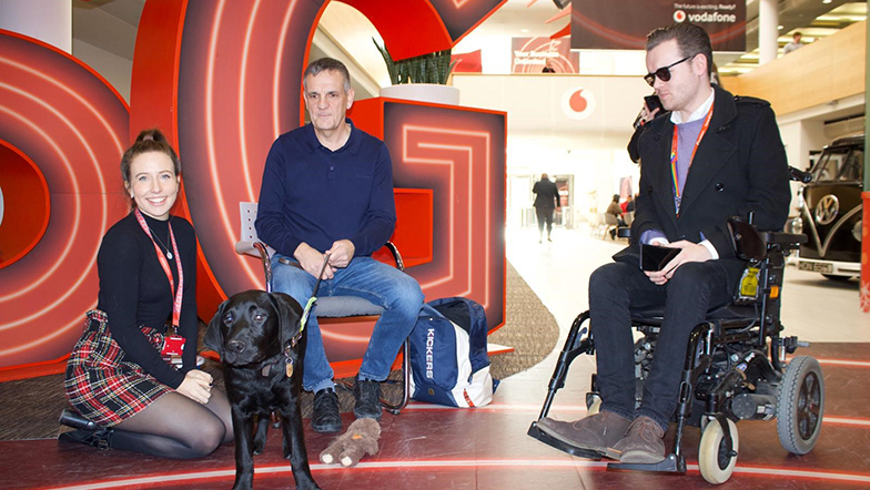 Vodafone staff sat with a guide dog owner and their black Labrador guide dog