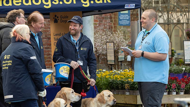 Guide Dogs fundraising volunteers with dogs at a stand