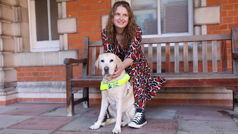 Guide dog owner sitting on a bench with her guide dog sitting at her feet