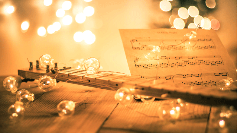 A guitar resting on a table surrounded by festive Christmas lights