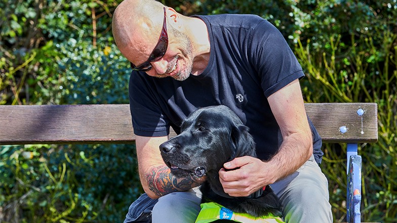Terry sat on a bench stroking his guide dog Spencer