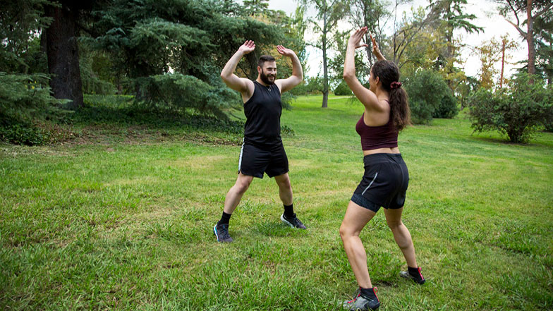 Two people taking part in a personal training session in a large green outdoor setting 