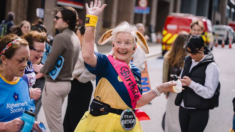 Runner wearing a Guide Dogs t-shirt and dog ears and waving as they run