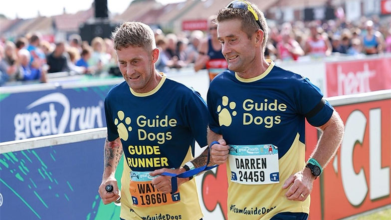 Runner Darren Swales with his sighted guide both wearing a Guide Dogs t-shirt
