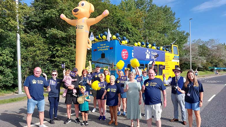 Event volunteers in Guide Dogs t-shirts in front of a bus with a Guide Dogs banner