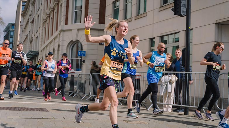 Runner at London Landmarks Half Marathon wearing a Guide Dogs vest and waving as they run past