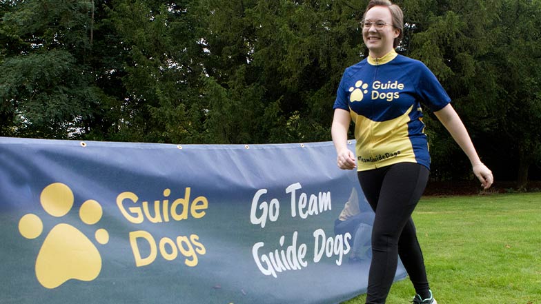 A person wearing a Guide Dogs t-shirt next to a Guide Dogs banner