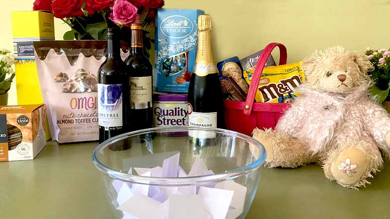 Raffle prizes such as chocolates, biscuits, teddy bears, plants, wine and champagne are displayed alongside raffle tickets in a bowl. 