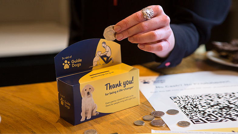 Someone putting in some change into a Guide Dogs coin collector