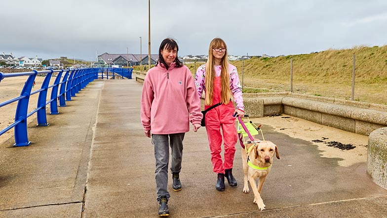 A guide dog owner with her dog and another person, walking along a path