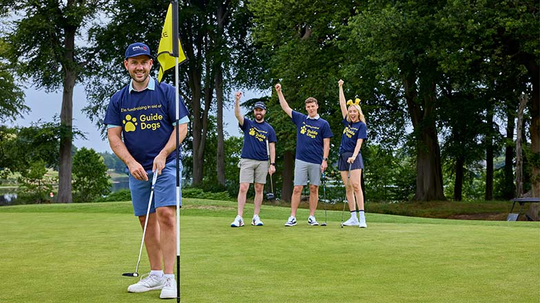 A man playing golf with three people people in the background cheering and all are wearing Guide Dogs T-shirts 