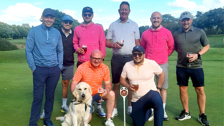 A group photo of people on a golf course with a dog wearing a Guide Dogs bandana