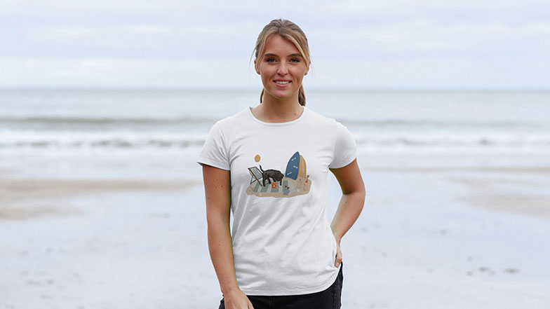 A woman is wearing a t-shirt with a dog on a beach design from the Laura Fisher and Guide Dogs collection