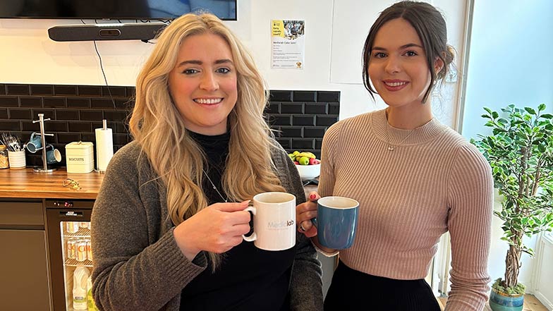 Two colleagues pictured smiling enjoying a cup of tea together.
