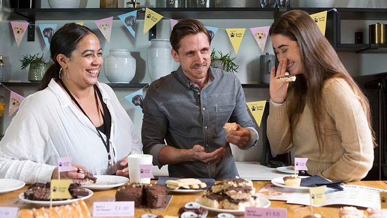 Three people smiling and laughing whilst at work eating cake.