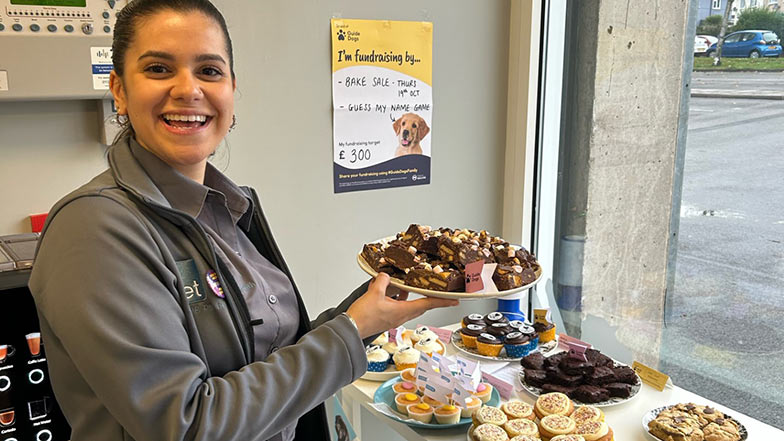 A person holds up a tray of cakes whilst fundraising at work. 