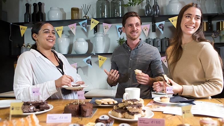 Image of three people smiling and laughing whilst at work eating cake.