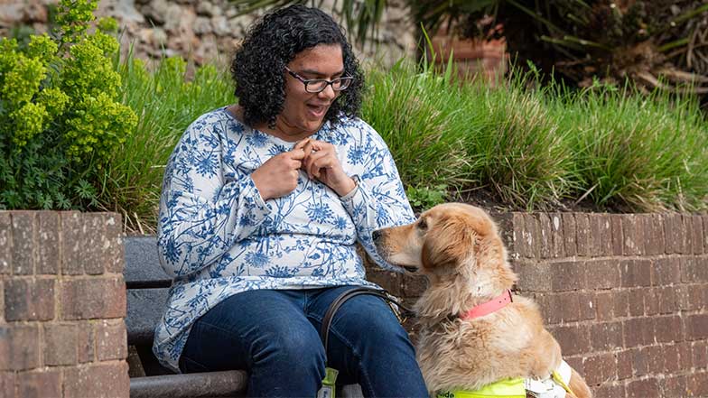 Smiling guide dog owner sitting on a garden bench with her golden retriever guide dog sitting patiently waiting for a treat.