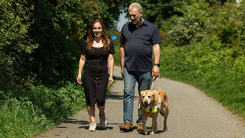 Mary and her father Simon walking together along a country path with guide dog Mayne.