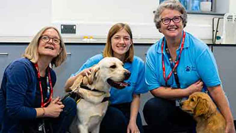 A group of Guide Dogs' Puppy Raisers smiling at the camera and cuddling their dogs
